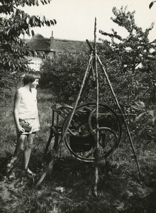 M 896 Een meisje in een kersenboomgaard en met een ratel bekijkt een oud werktuig