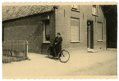 4-803 Een mevrouw met een fiets in de hand buiten staand voor een huis.