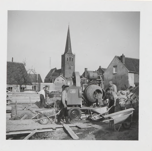 0362-662 Cement wordt uit betonmolen in kruiwagen gegoten. Werklui in de weer. Op achtergrond o.a. N.H.-kerk