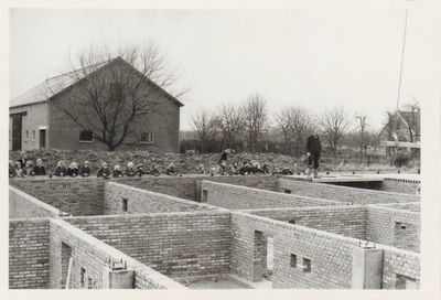 0362-842 Kinderen kijken toe bij plaatsing vloerdelen school. Op achtergrond links: schuur Huize 'De Kamp', rechts: ...