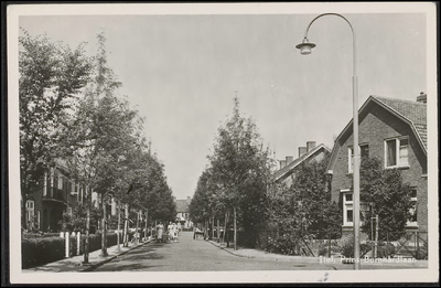 B 4.2 Straat met eengezinswoningen, bomen, lantarenpaal op de hoek en vrouwen op de straat.