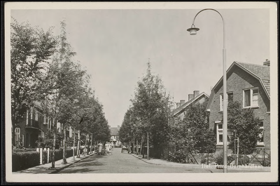 B 4.4 Straat met eengezinswoningen, bomen, lantarenpaal op de hoek en vrouwen op de straat.