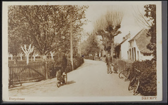 D 4.4 Reproductie. Straat rechts huizen links boomgaard. In de straat man met kind en een man op de fiets.