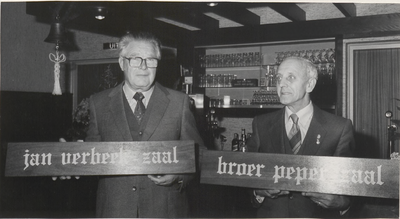 M 3394 De heren Jan Verbeek, links, en Broer Peper, rechts, met de borden van de naar hen genoemde zalen in het Gustaaf ...