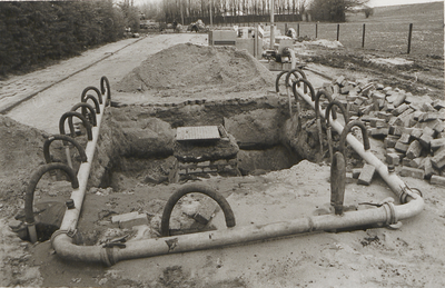 M 5393 Aanleg nieuwe riolering in Nachtegaallaan. Op de voorgrond een put in het wegdek. Het buizen- en slangenstelsel ...