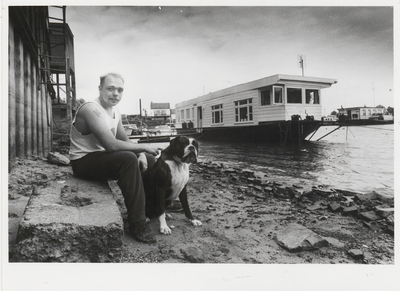 M 6722 Op de foto een man met zijn hond die zit bij de haven zit waarschijnlijk is rechts zijn woonboot