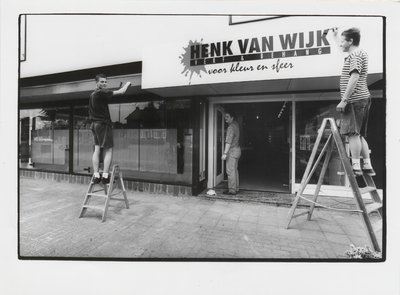 M 7277 Foto van het ophangen van een reclamebord bij het pand van Henk van Wijk verf en behang, voor kleur en sfeer aan ...