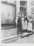 M 8040 Man met pet en drie vrouwen in schort voor een winkelpand, ws. jaren 20-30