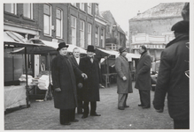 M 8275 Markt op Plein. Links de gemeenteboden v.l.n.r.: Piet Hevel, onbekend, Arie van Mourik. Op de achtergrond rechts ...
