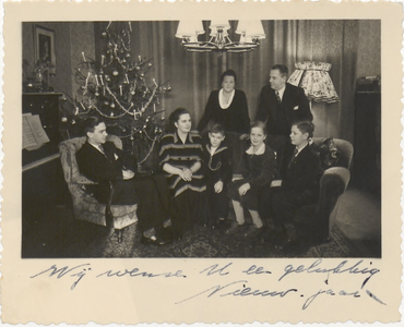 M 8995 Gezinsfoto, zeven personen w.o. drie kinderen in een huiskamer met kerstboom, handgeschreven nieuwjaarswens ...