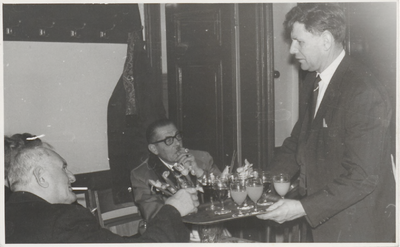 M 9055 Ober serveert drankjes aan twee mannen in een zaaltje.