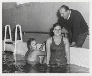 M 9074 Twee dames staand in zwembad, op de kant een bukkende man