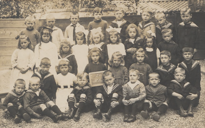 M 9140 Groepsfoto van een schoolklas, op een lei staat 1e klas, veel jongens met matrozenpakjes, meisjes met grote strikken.