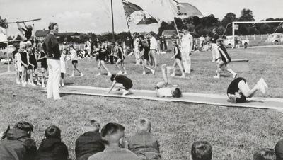 M 9270 Waarschijnlijk turndemonstratie op schooldag op een voetbalveld, twee vlaggen, aantal meisjes doet oefeningen op ...