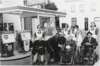 M 9540 Chevron benzinestation, vor de pimpen enkele personen in invalidenwagens, daarachter verpleegsters