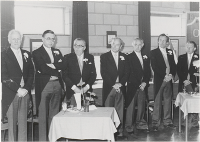 M 9718 Groep van zeven heren in jacquet, met corsage, staand in een ruimte