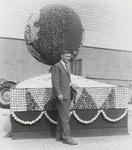 M 9928 Man voor versierde praalwagen met bol, mogelijk een van de eerste fruitcorso's