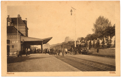 1085 Een prentbriefkaart van de achterzijde van het spoorwegstation in Tiel met reizigers en een locomotief met rijtuigen