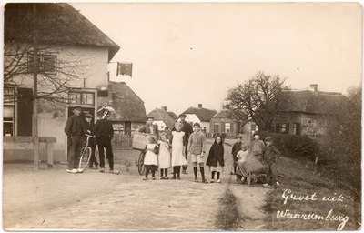 1102 Een prentbriefkaart van een straat in Waardenburg met poseren kinderen en volwassenen met links een uithangbord ...