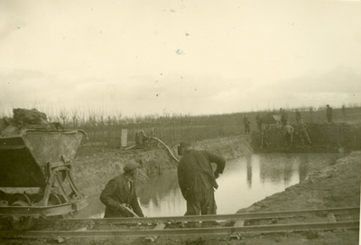 1086 Mobilisatie Kesteren en omgeving: groep mensen bezig met kuil afgraven en afwateren; op de voorgrond een rail met kar