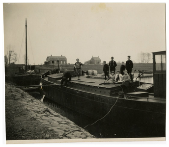 4-792 Een groep personen staande op een boot die afgemeerd ligt in de haven, op de achtergrond het Oude Veerhuis.