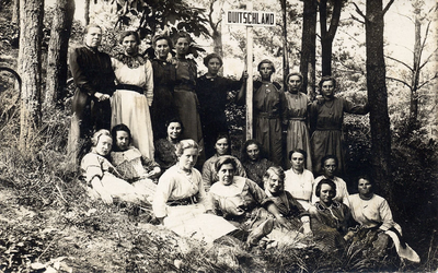 16-188 Een groep vrouwen buiten in een bos een van hen draagt een bordje met daarop het woord Duitschland. Te herkennen ...