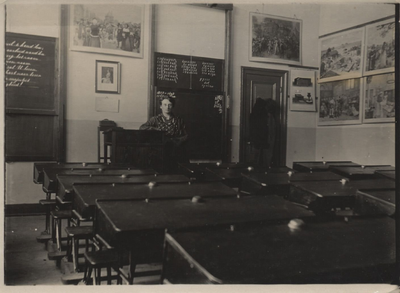 21-161 Juffrouw Six Dijkstra, juffrouw aan de christelijke lagere school 1922-1934, achter haar lessenaar in de klas ...