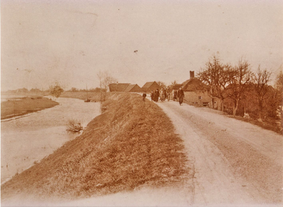 21-337 Een groepje mensen lopend over de dijk langs het water met aan de dijk ook nog wat huizen zichtbaar.