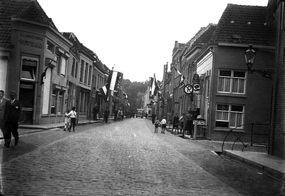 22-8828 Straatgezicht richting Bossche Poort, vlaggen hangen uit. Links hoekhuis Geldersche slagerij J. van Oosterom