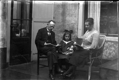 22-9558 Familie op een terras, een man en een vrouw zitten te lezen met tussen hen in een kind met een pop